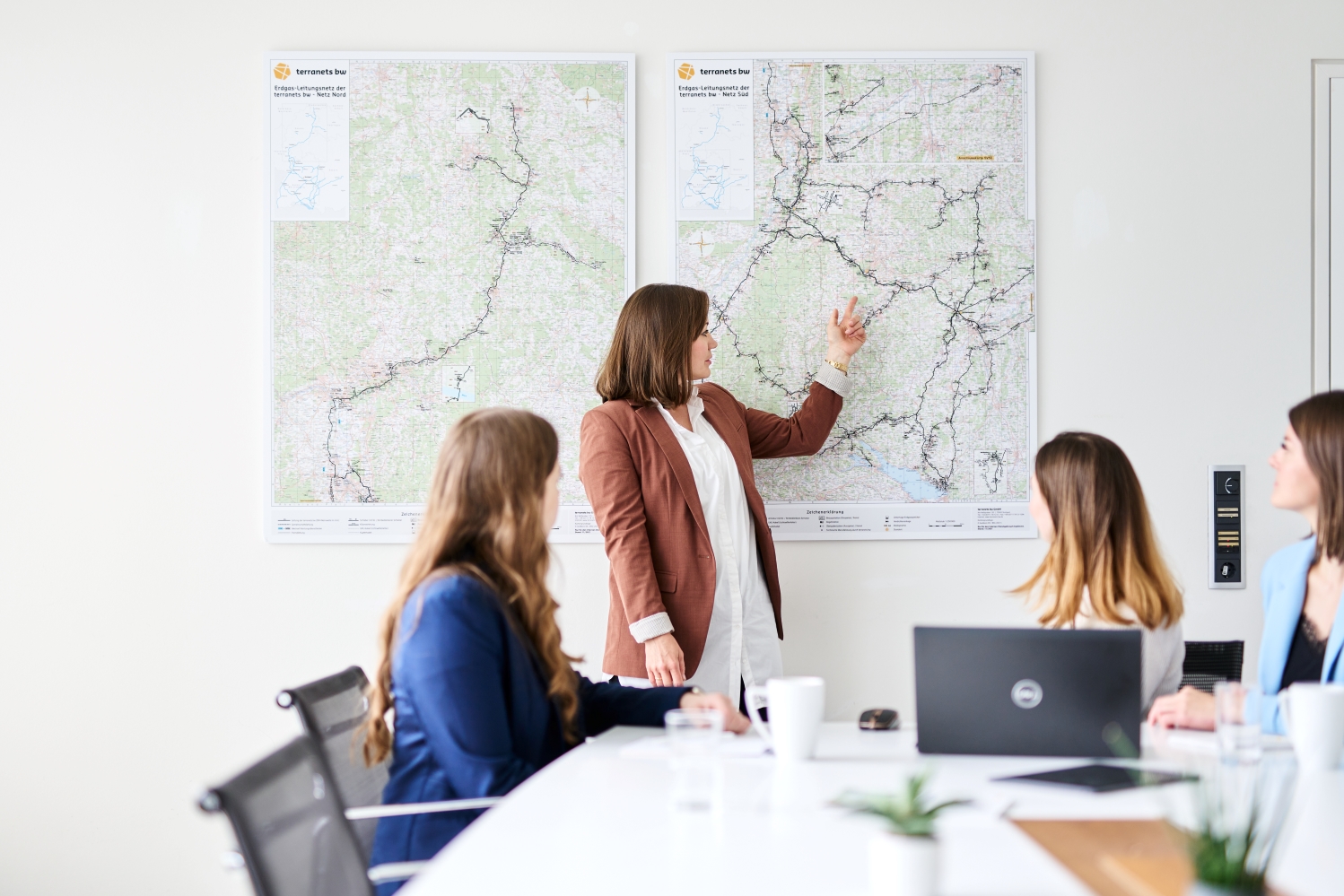 Drei Mitarbeiterinnen von terranets bw im Workshop, eine Person zeigt den anderen Personen etwas auf einer Netzkarte, ein Laptop und eine Tasse auf dem Tisch